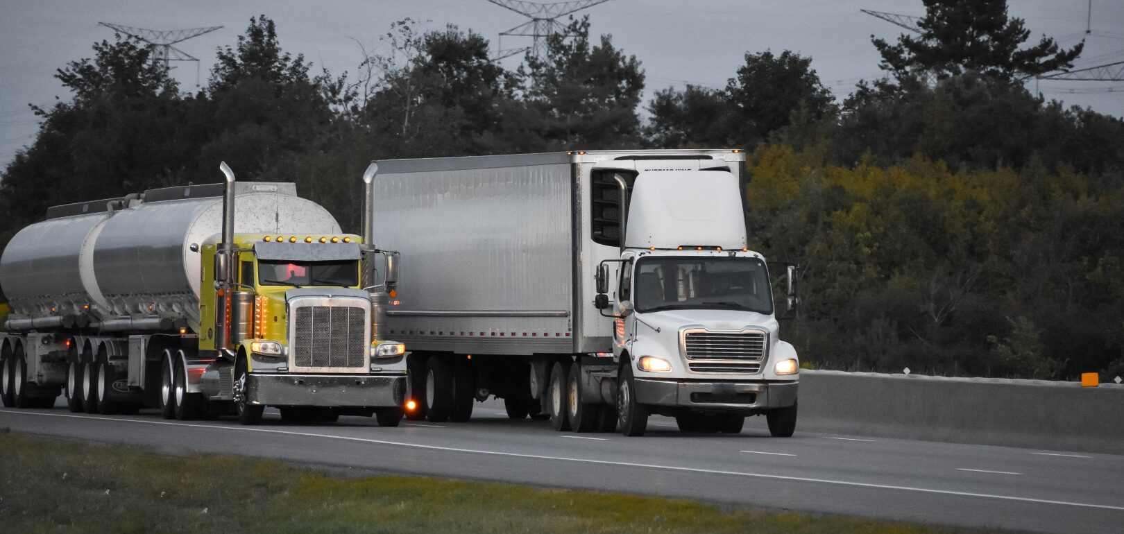 Two trailer trucks driving on the road surrounded by beautiful green trees
